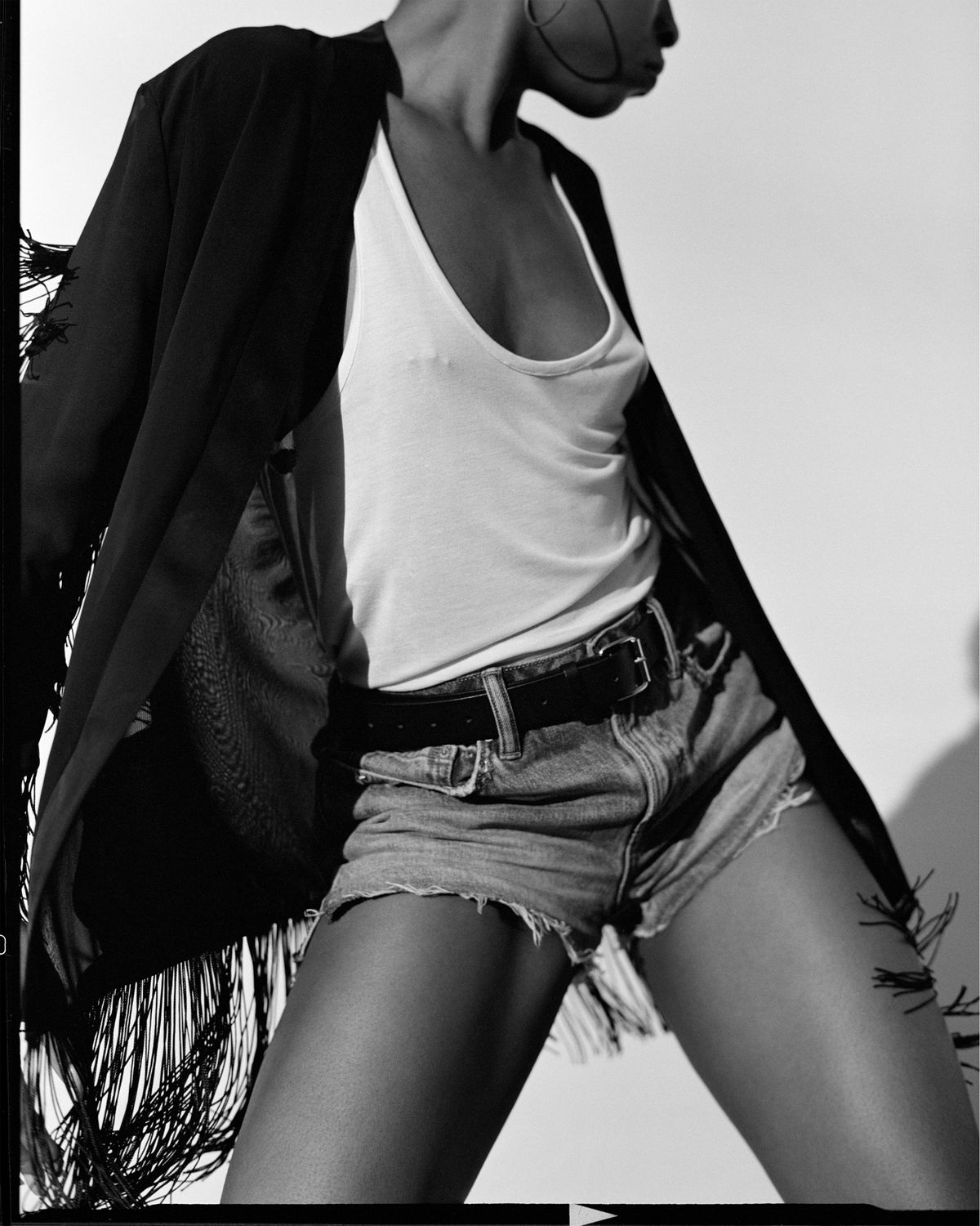 Fotografía en blanco y negro de una chica en movimiento vistiendo un kimono negro con flecos encima de una camiseta blanca y shorts de denim.