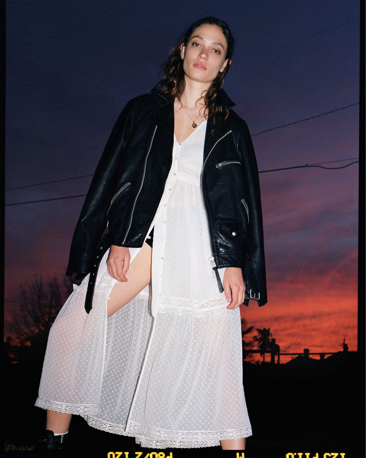 Fotografía de una chica posando al atardecer, vistiendo un vestido largo de topos de nuestra última colección y una cazadora de cuero negro.