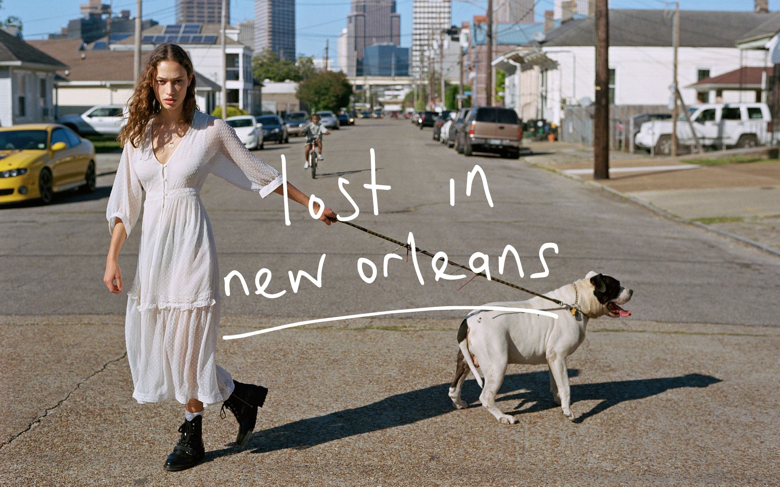 Fotografía de un paisaje tomada en las calles de Nueva Orleans donde aparece una chica paseando a un perro con un vestido blanco largo de nuestra última colección de verano.