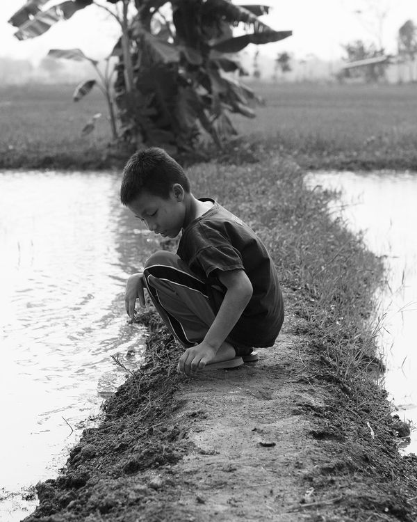 Black and white photo of a street kid playing next to water.