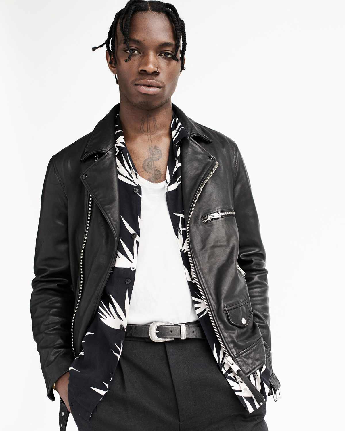 Portrait of a young man wearing a leather biker jacket and a printed shirt from our latest collection, layered over a white t-shirt and black tailored trousers.