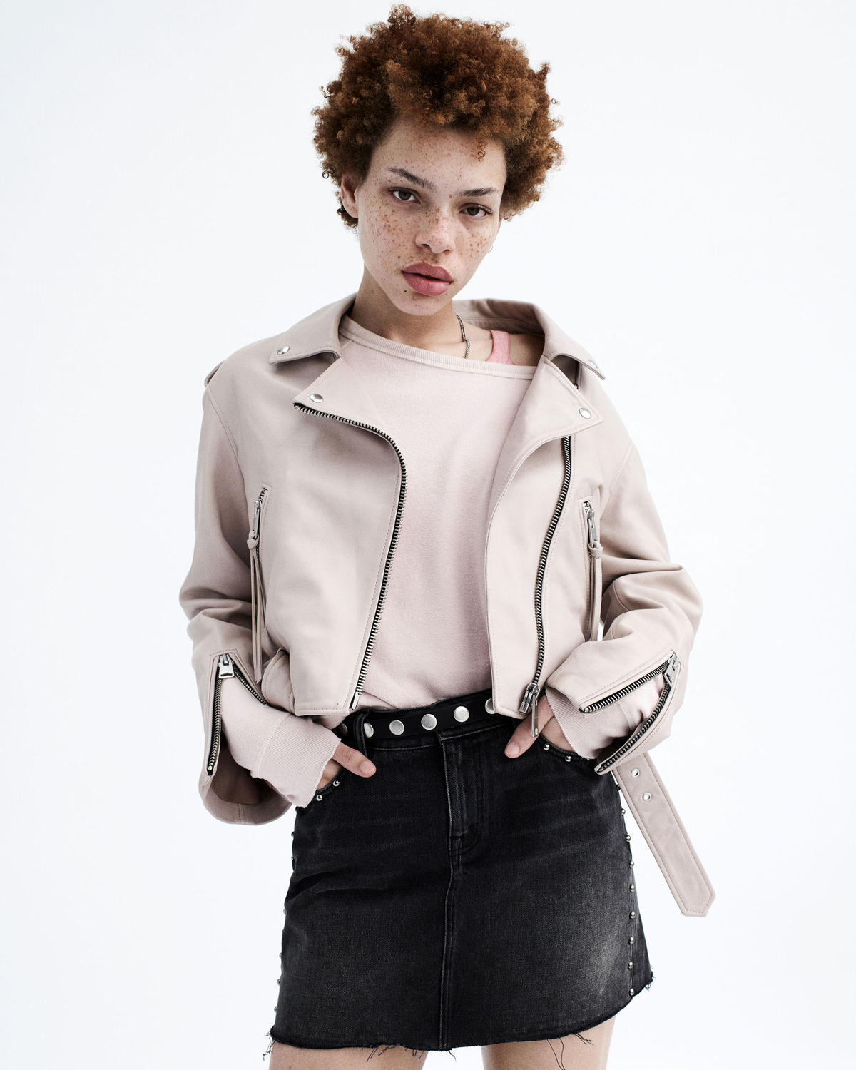 Portrait photograph of a young woman wearing a studded black denim skirt and a pink t-shirt, layered under a washed pink biker jacket.
