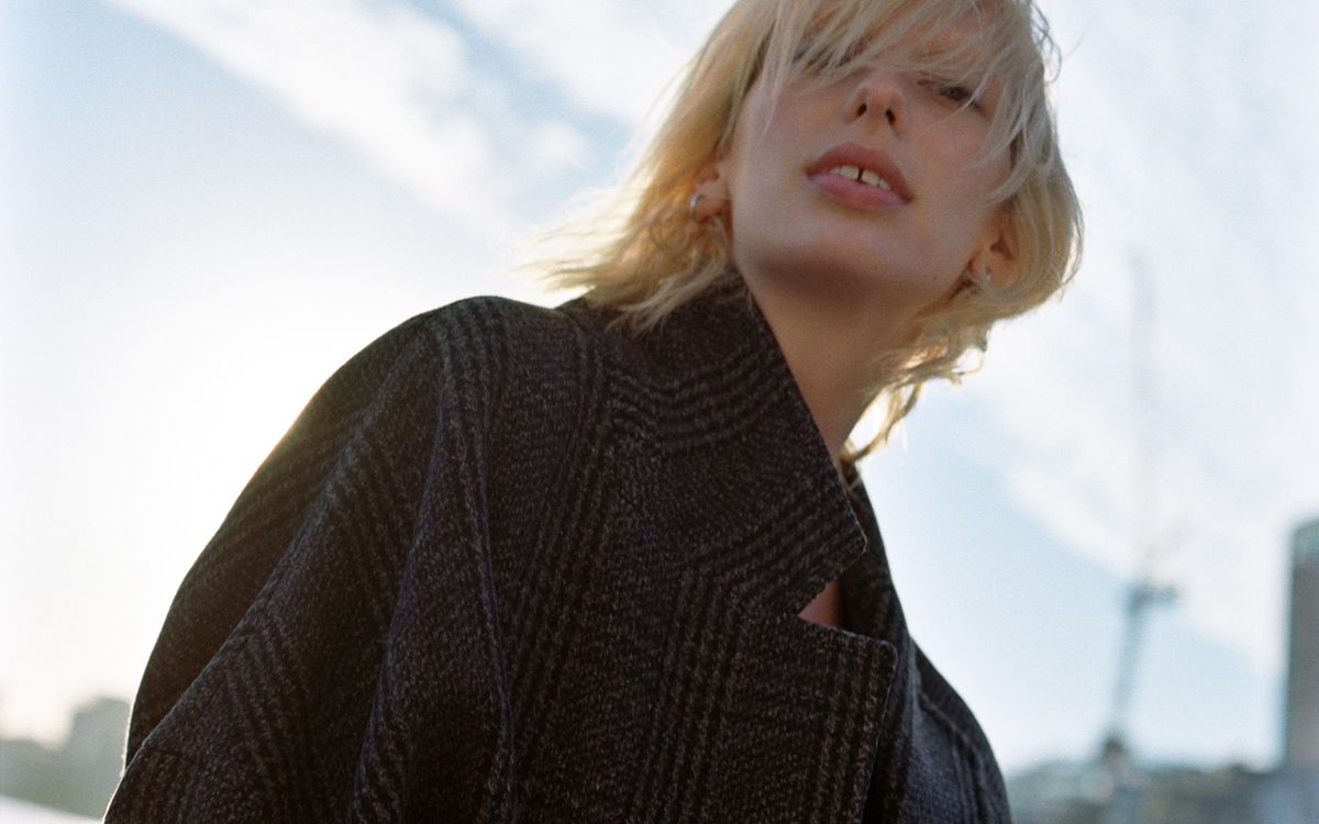 Close up of a woman looking at the camera and wearing a checked oversized coat.