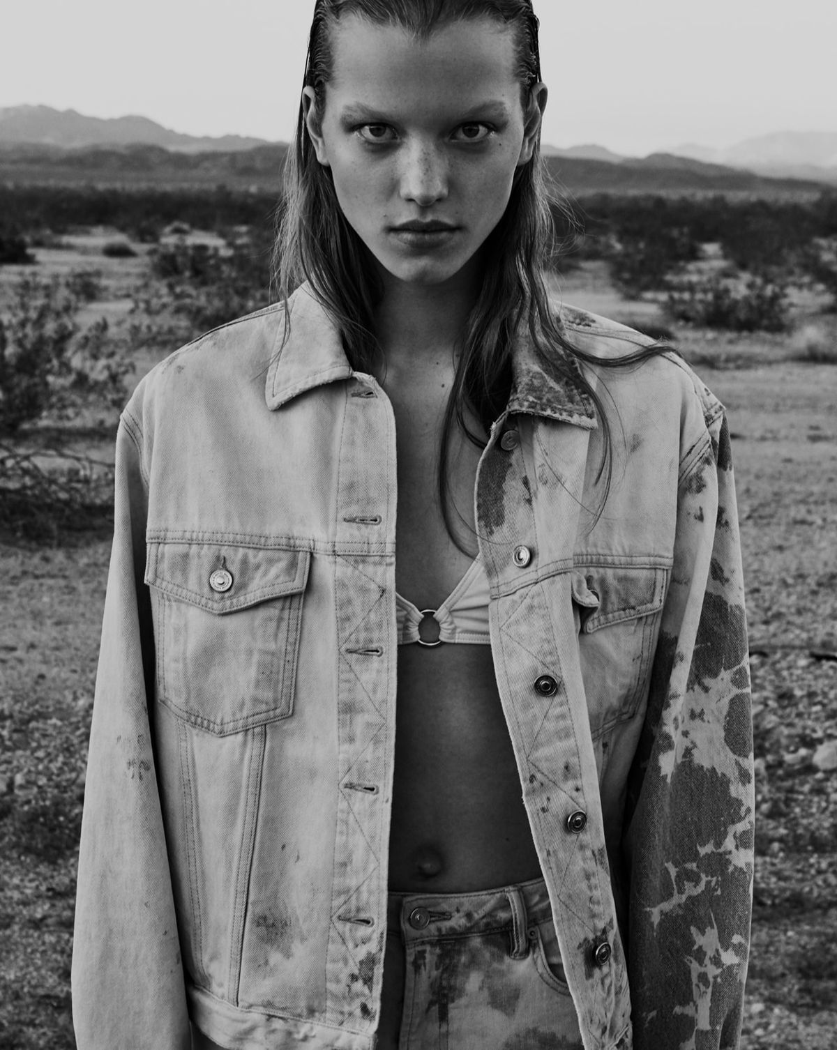 Black and white image of a woman wearing a bleached denim jacket with matching jeans and a bikini top.