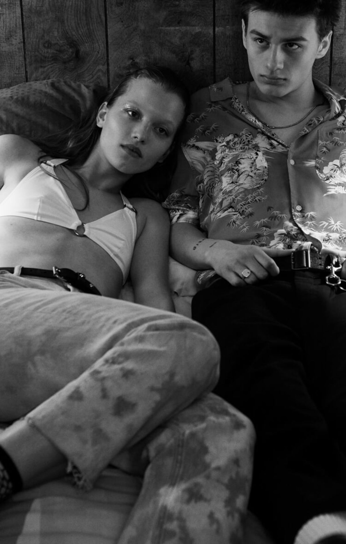 Black and white image of a man and a woman lying on a bed wearing outfits from our latest collection.