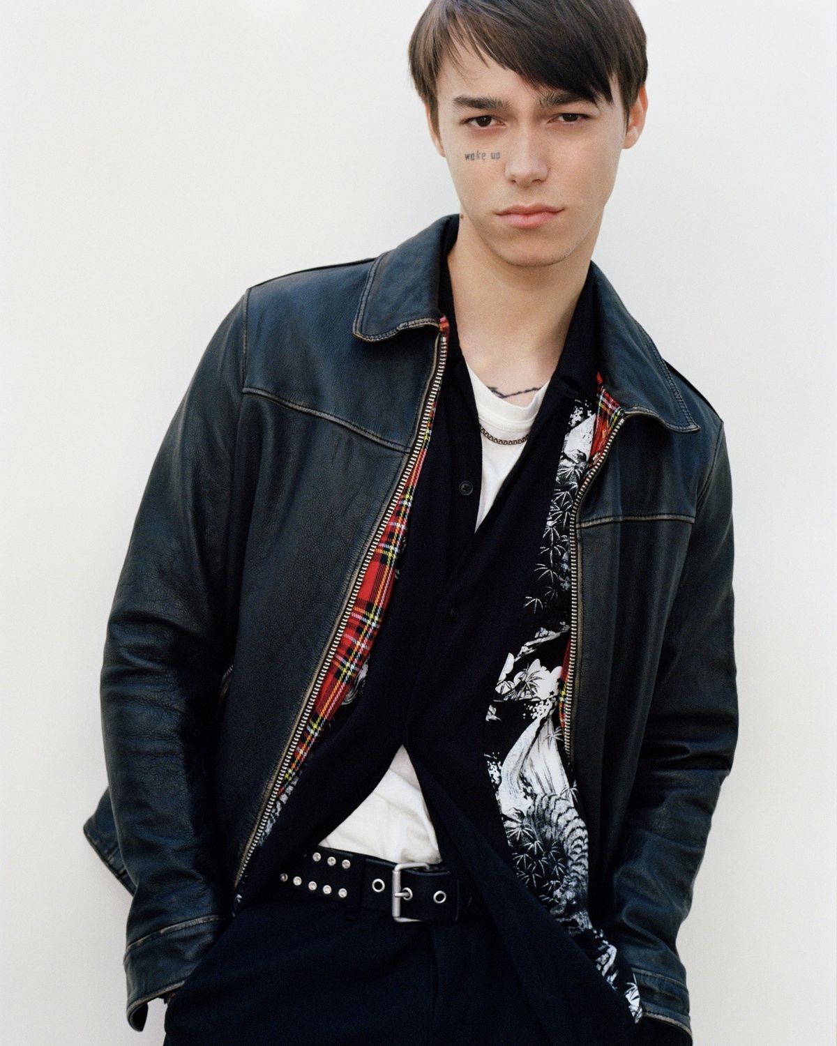 Portrait of a man staring at the camera and wearing a black vintage style biker jacket over an opened printed shirt and white t-shirt.