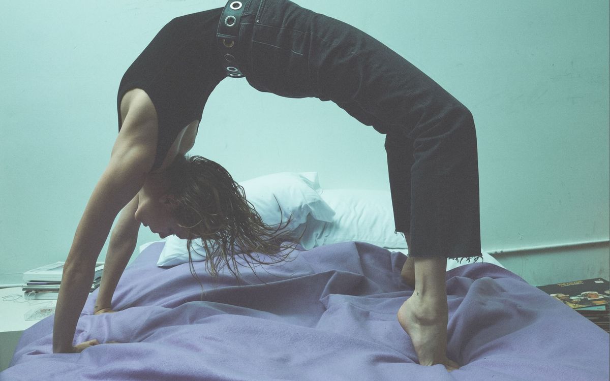 Landscape picture of a woman doing a bridge pose on top of a bed.