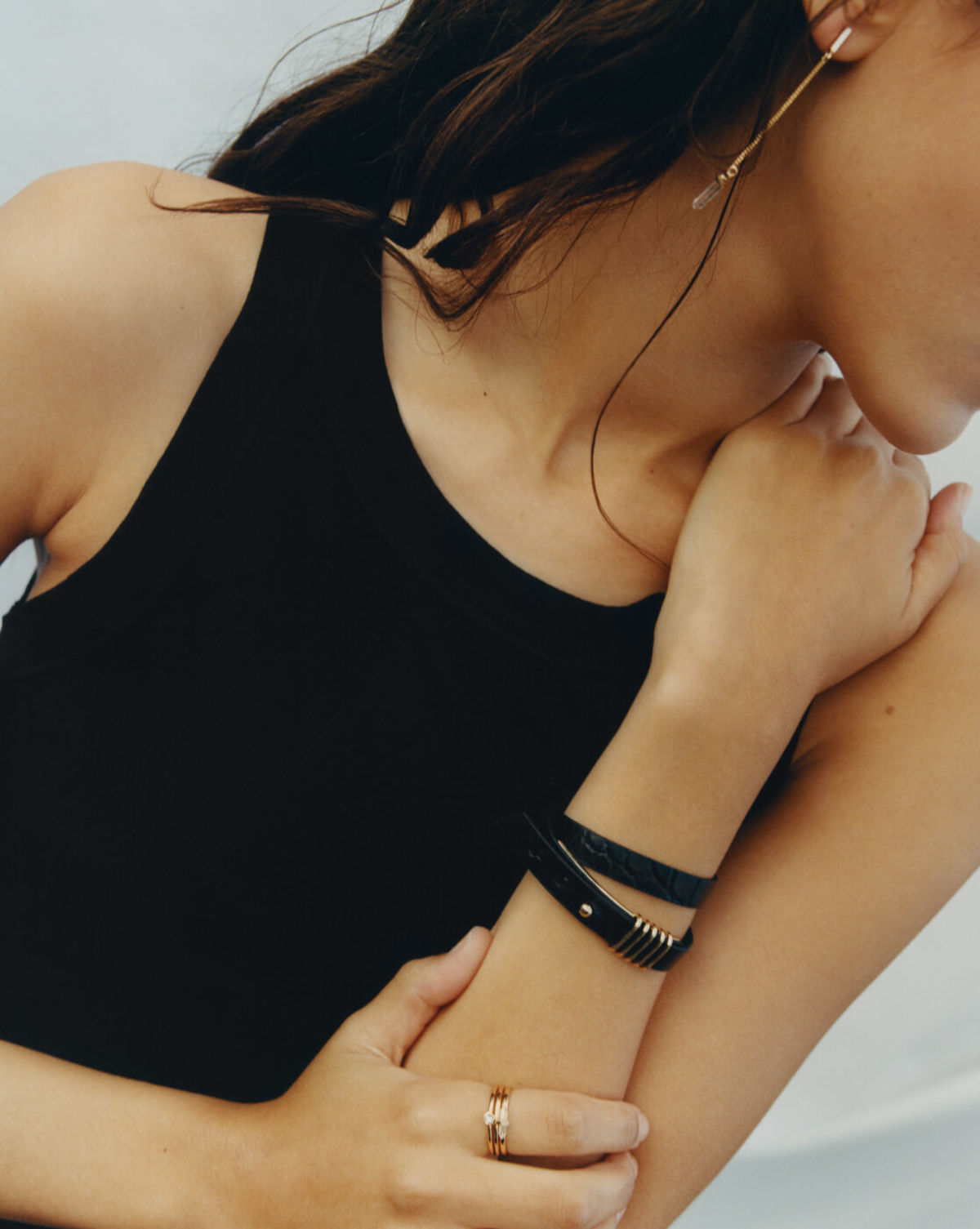 Close up of a woman wearing a black tank top and displaying a bracelet and a set of rings and earing from our latest jewellery collection.