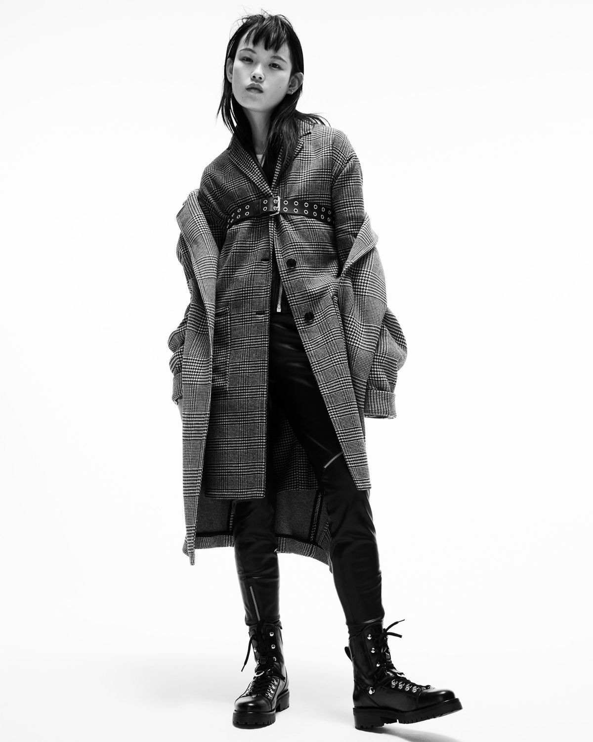 Black and white image of a woman wearing a leather jacket and two checked coats in layers.
