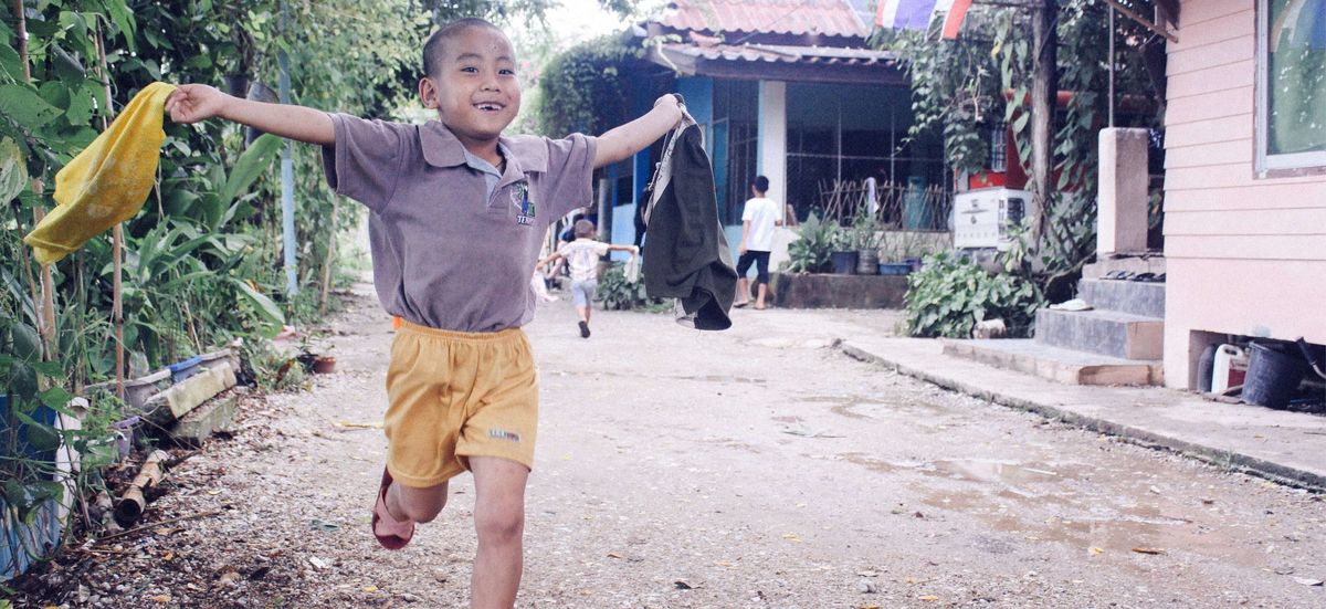 Kind läuft auf der Straße mit einem breiten Lächeln und offenen Armen.