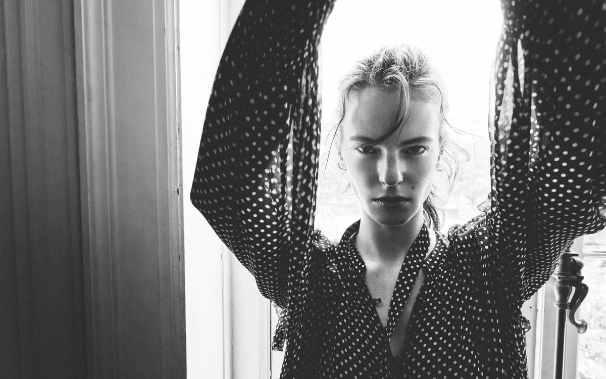 Black and white image of a woman staring at the camera and wearing a polka dot shirt.