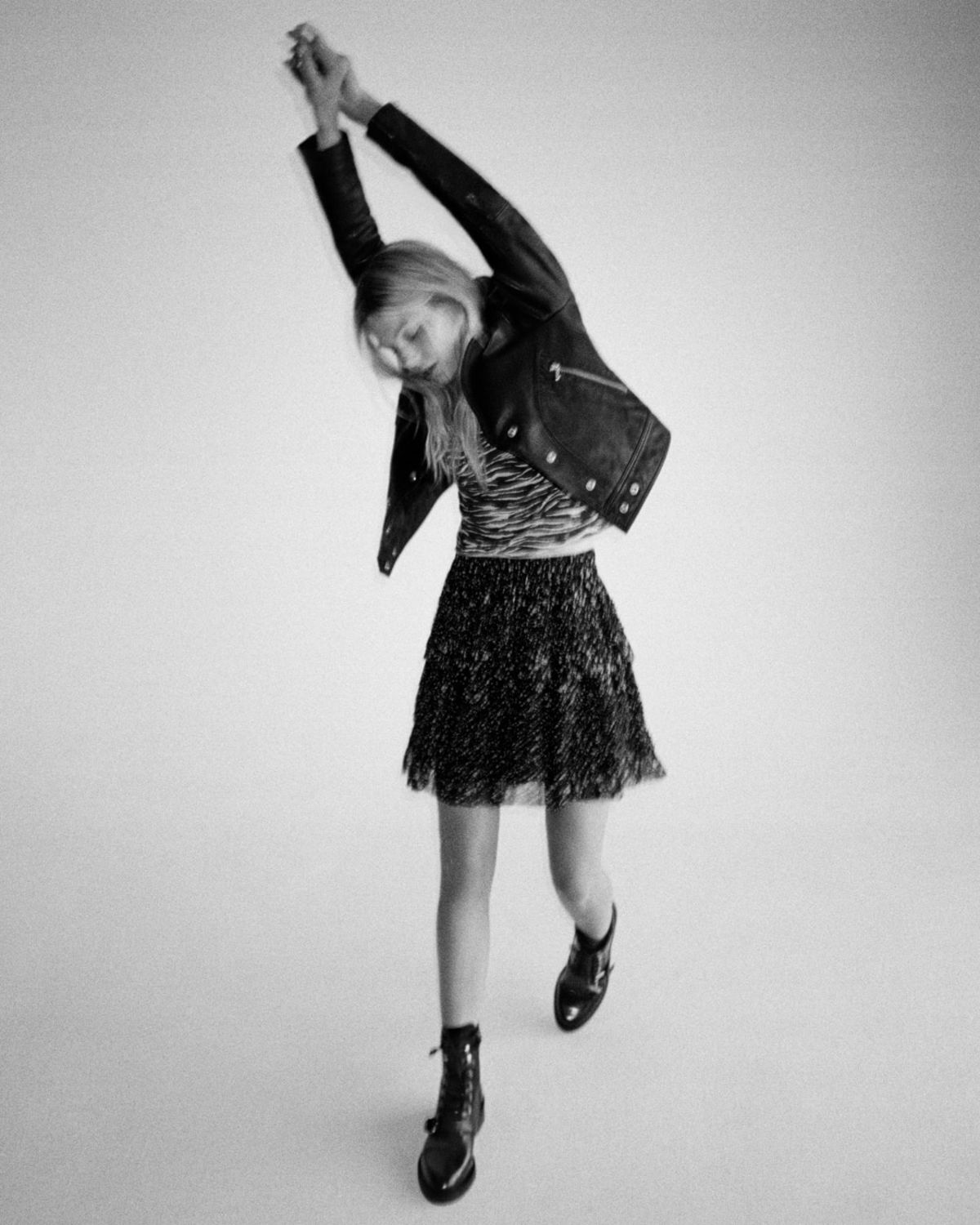 Black and white image of a woman wearing a black leather biker jacket over a zebra printed t-shirt and a floral skirt.