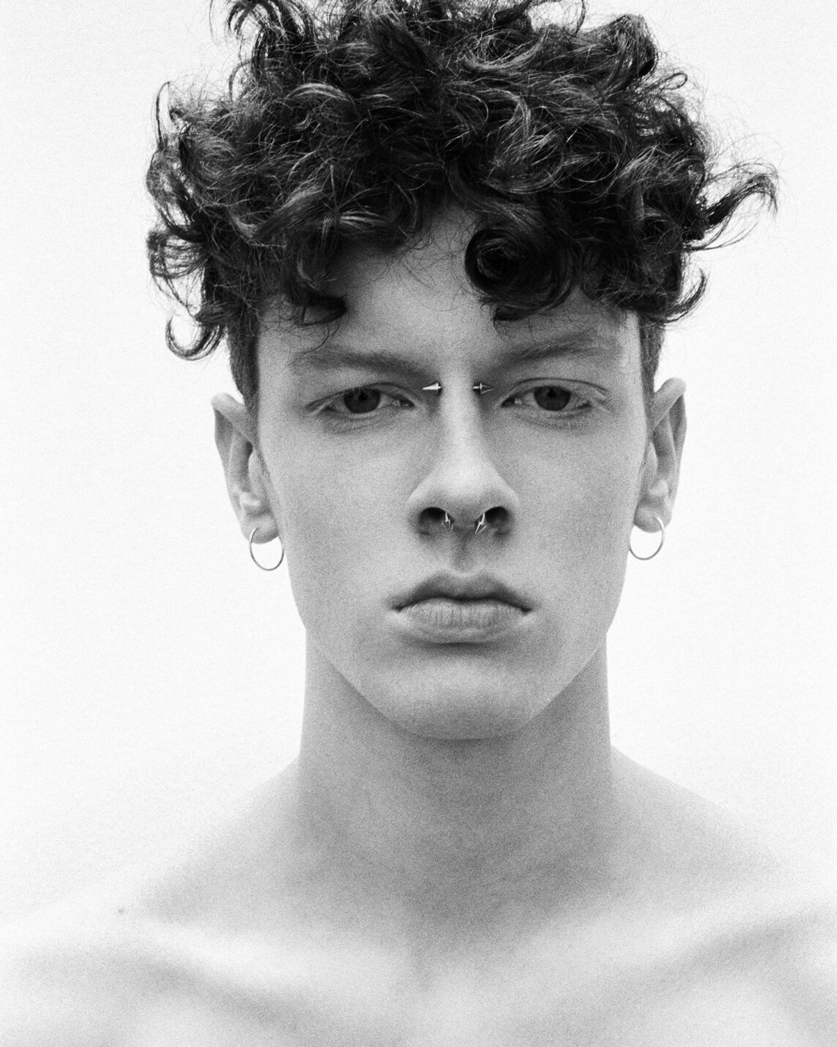 Black and white portrait of a man with a couple of piercings on his nose and earings.