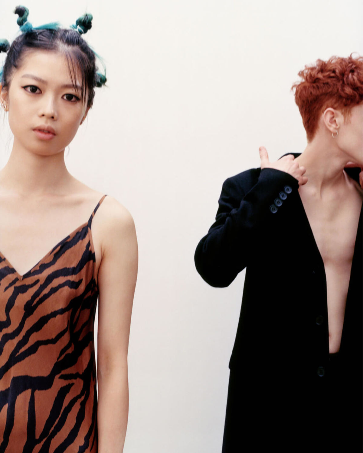 Image of a woman wearing an orange zebra printed dress and a man in the background wearing a black blazer and pants.