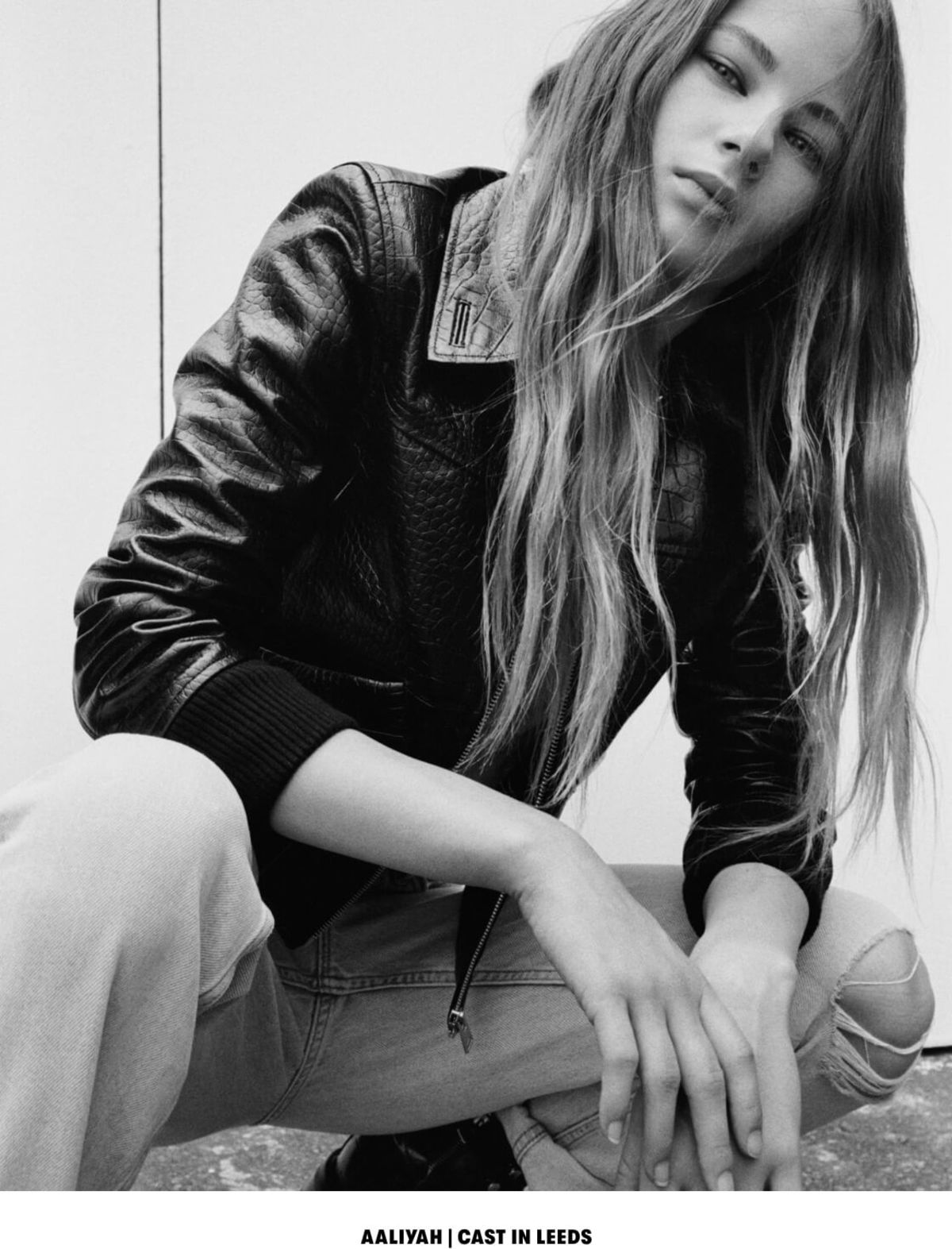 AALIYAH | CAST IN LEEDS. Black and white image of a woman wearing a black snake printed bomber with a white t-shirt and light denim jeans.