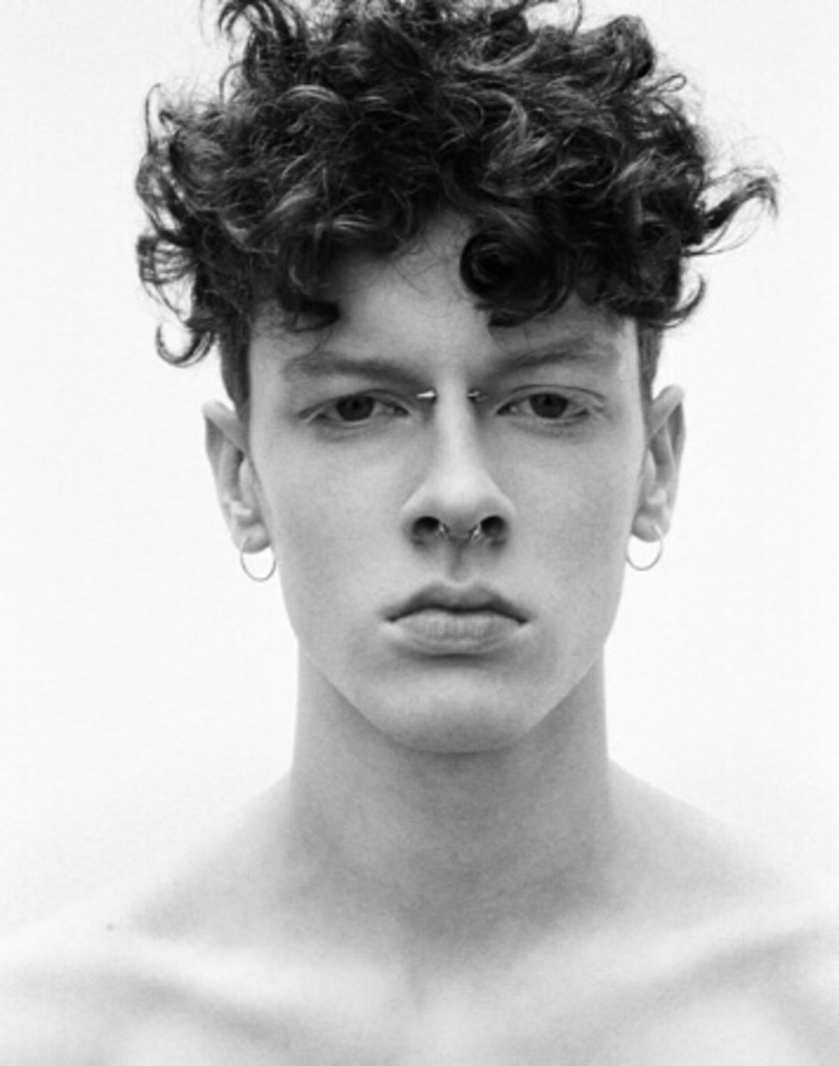 Black and white portrait of a man with a couple of piercings on his nose and earings.