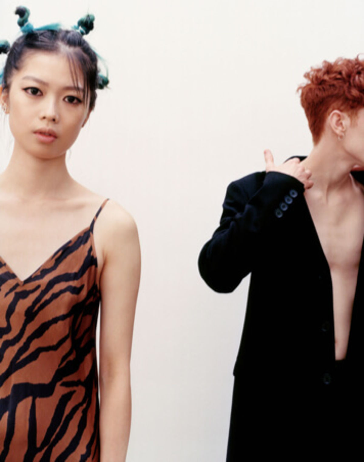 Image of a woman wearing an orange zebra printed dress and a man in the background wearing a black blazer and pants.