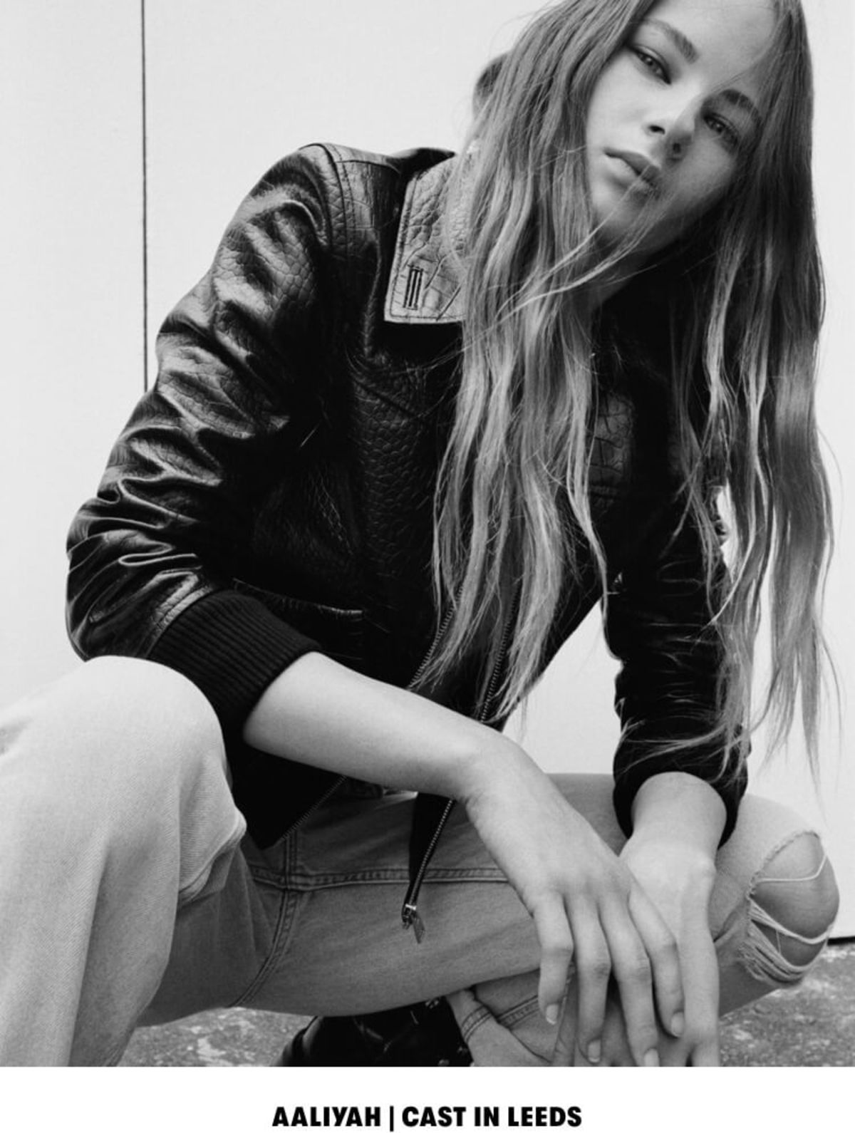 AALIYAH | CAST IN LEEDS. Black and white image of a woman wearing a black snake printed bomber with a white t-shirt and light denim jeans.