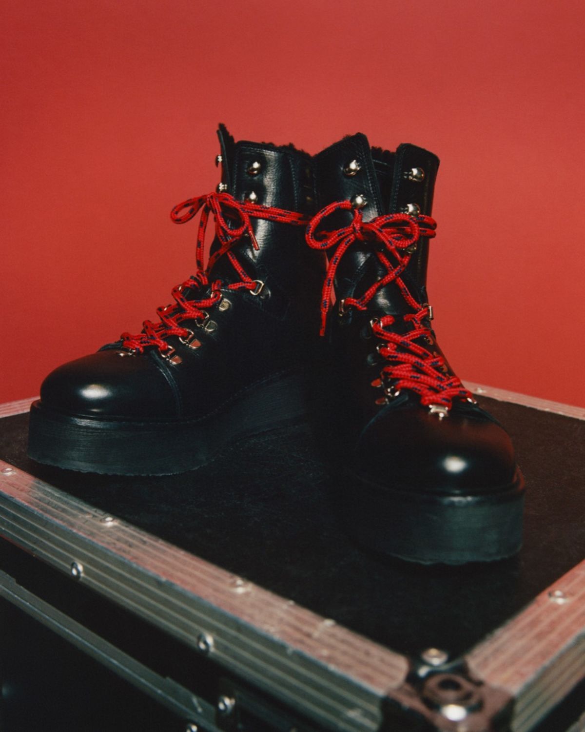 Close up of black leather military style shoes with red laces in front of a red background.