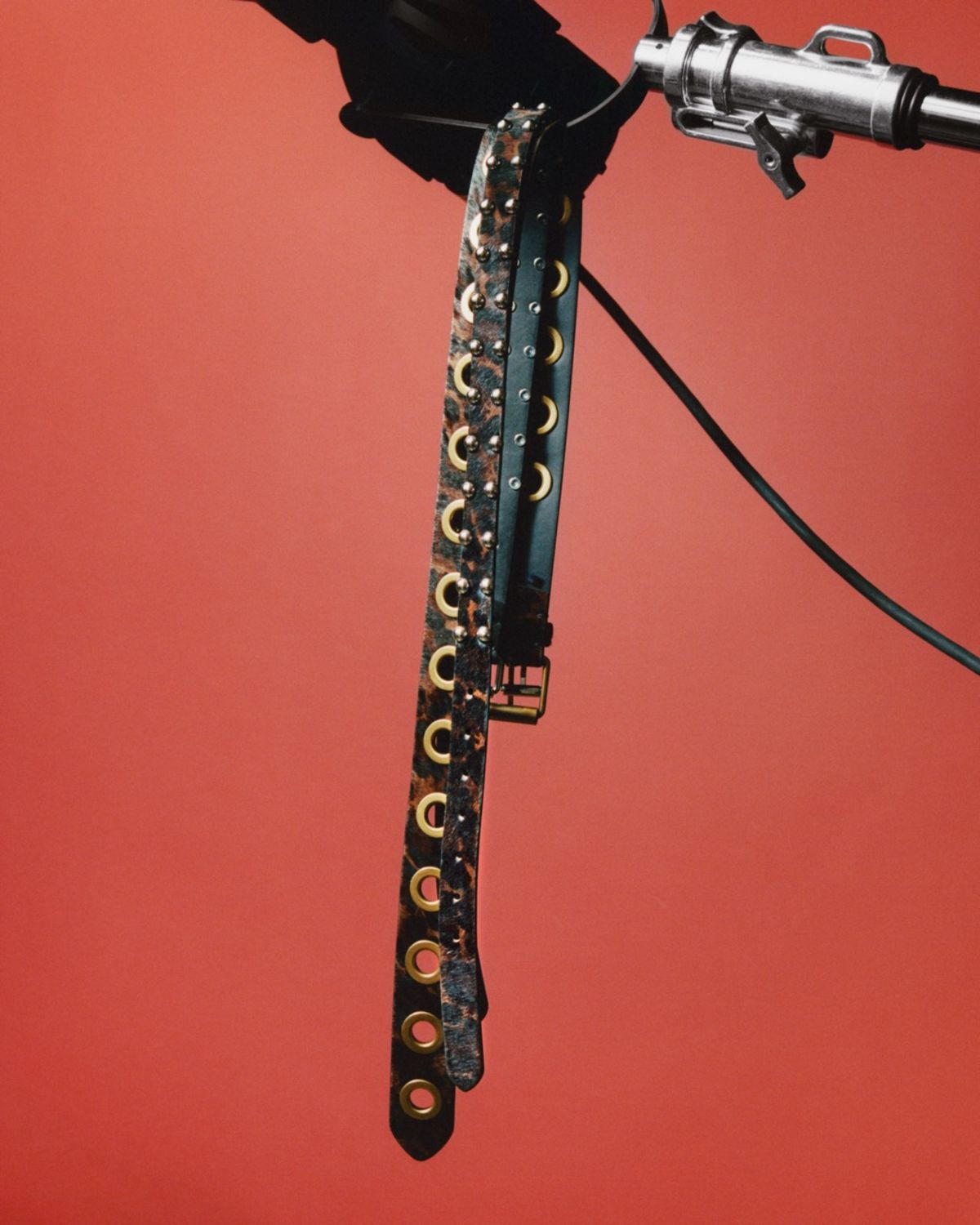 Close up of a few of our black and leopard printed leather belts hanging in front of a red background.