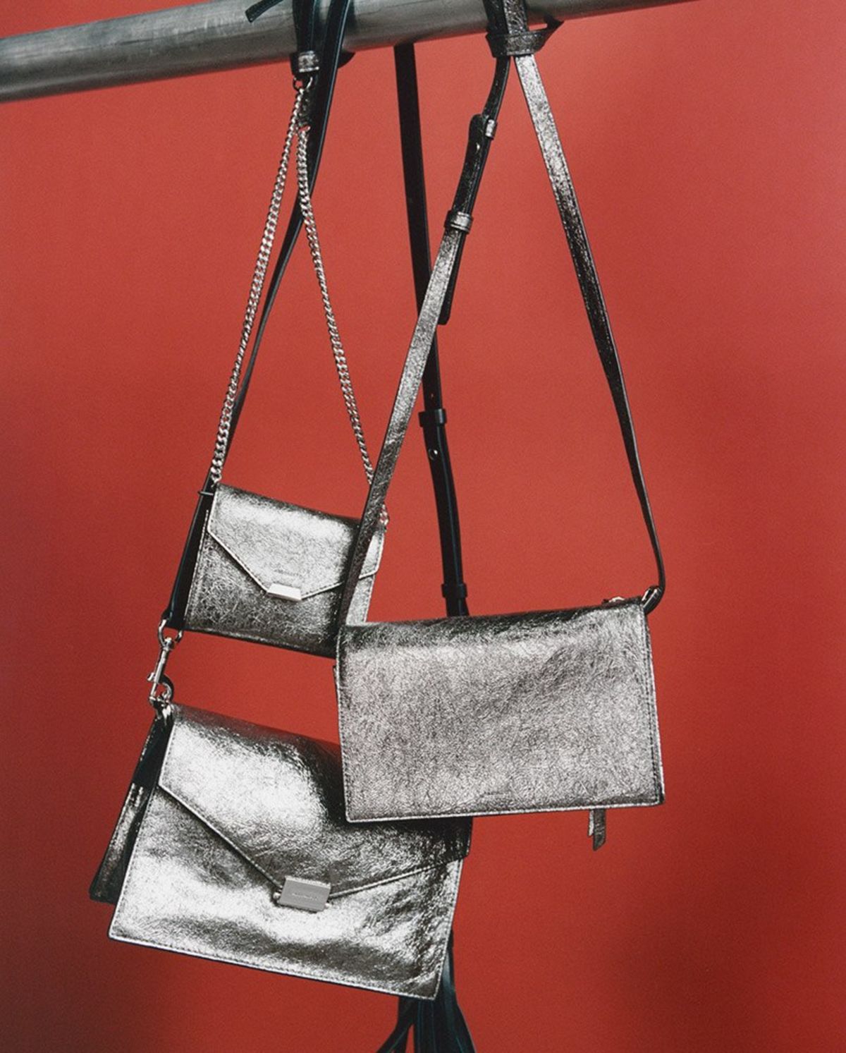 Imagen de tres bolsas de piel metalizada atadas a una estructura metálica frente a un fondo rojo.