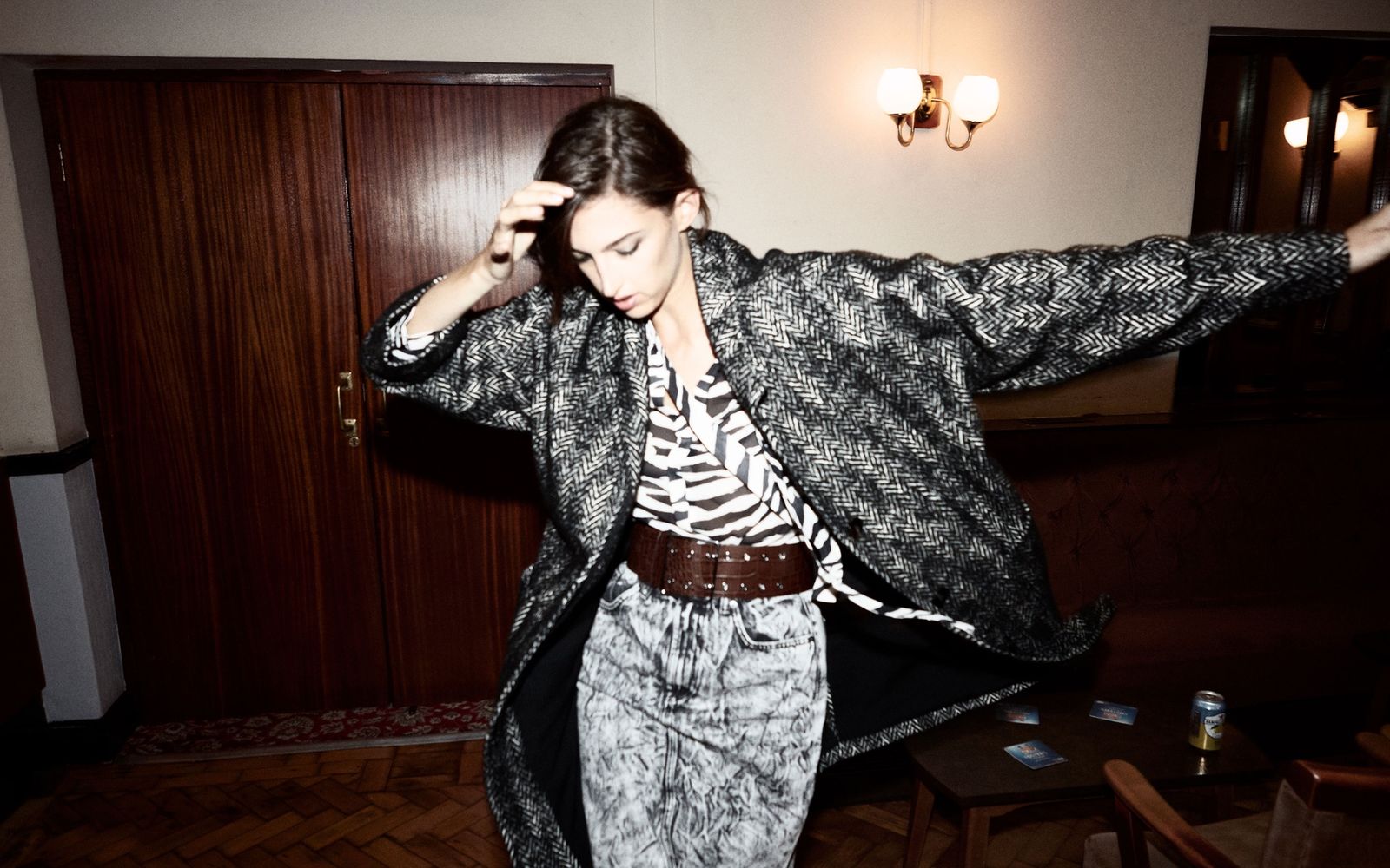 Immagine di una donna in un corridoio. Indossa una gonna a matita in tessuto texturizzato con una cintura marrone in pelle, una camicia zebrata e un cappotto nero e bianco.
