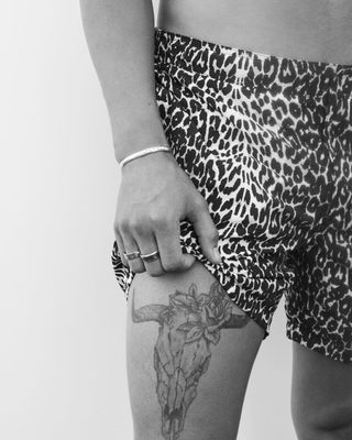 Inquadratura in bianco e nero di un uomo che mostra un tatuaggio Ramskull sulla coscia. Indossa un costume a pantaloncino con una stampa leopardata.