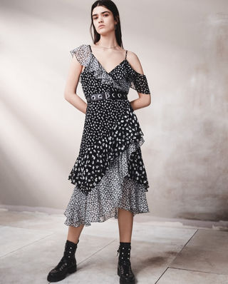 Image of a woman standing in front of a grey wall wearing a black and white printed floral dress with a leather belt and black leather boots.