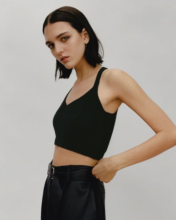 Woman wearing a black knitted crop top and a highwaisted leather-like trousers.