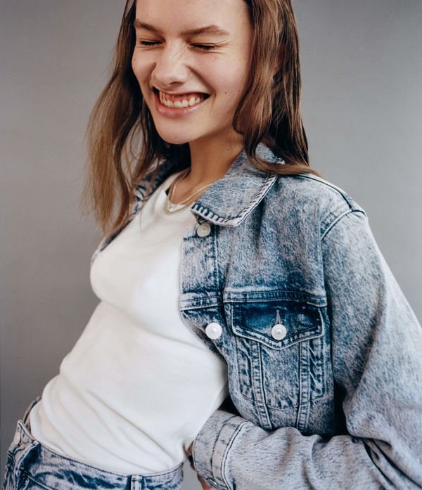 A smiling woman wearing blue jeans and a denim jacket.