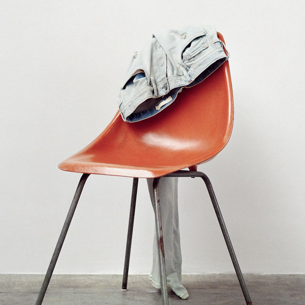 Pair of light grey jeans hanging at the back of an orange chair.