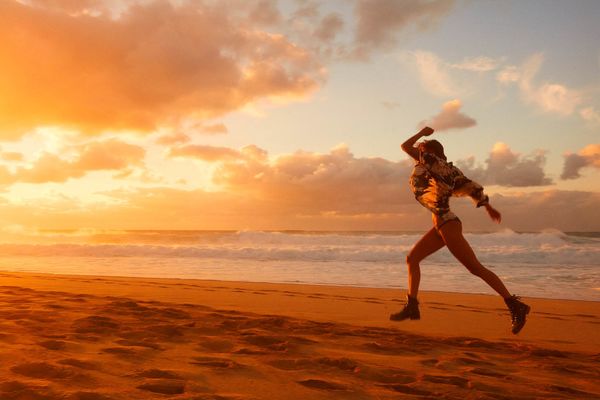 Landscape picture of a woman runinng on the beach with a sunset in the background.