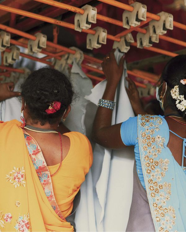 Deux femmes Indiennes se tiennent dos à l'objectif et détachent des pièces de cuir d'un séchoir.