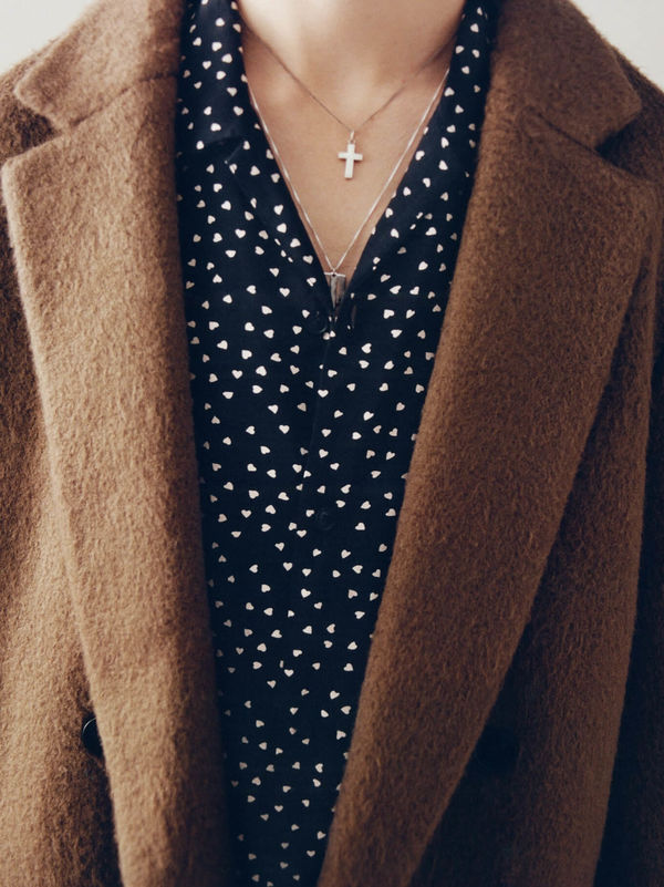 Man wearing a black and white printed shirt underneath a brown tailored coat.