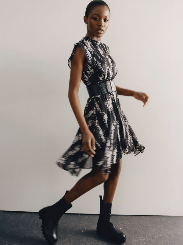 Woman wearing a black and white printed dress with a large black leather belt buckled on her waist.