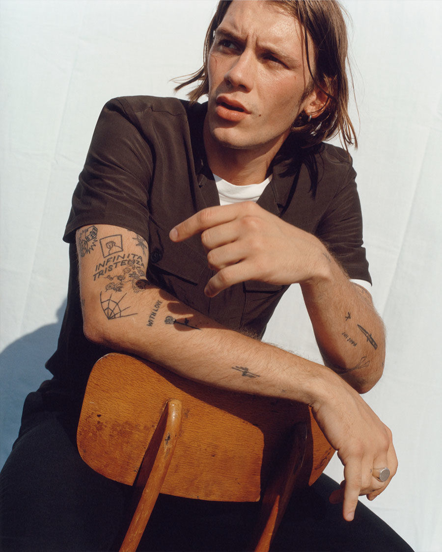 Image of a man seating on a wooden chair and wearing pieces from our latest collection.
