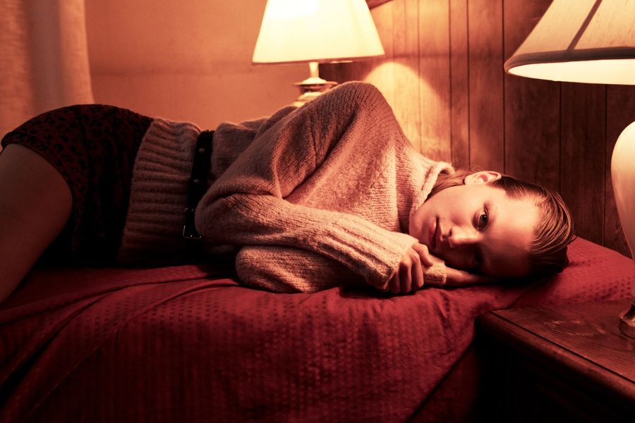 Immagine di una donna stesa sul letto della camera di un hotel. Indossa un maglione rosa con una gonna leopardata.