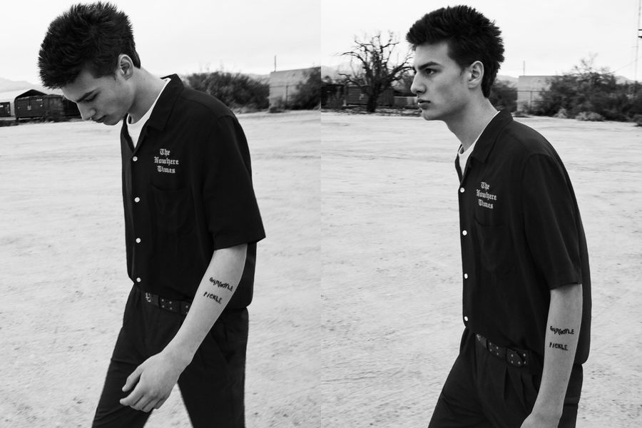 Due ritratti in bianco e nero di un uomo che cammina con indosso pantaloni neri sartoriali abbinati ad una camicia nera aperta su una t-shirt bianca.