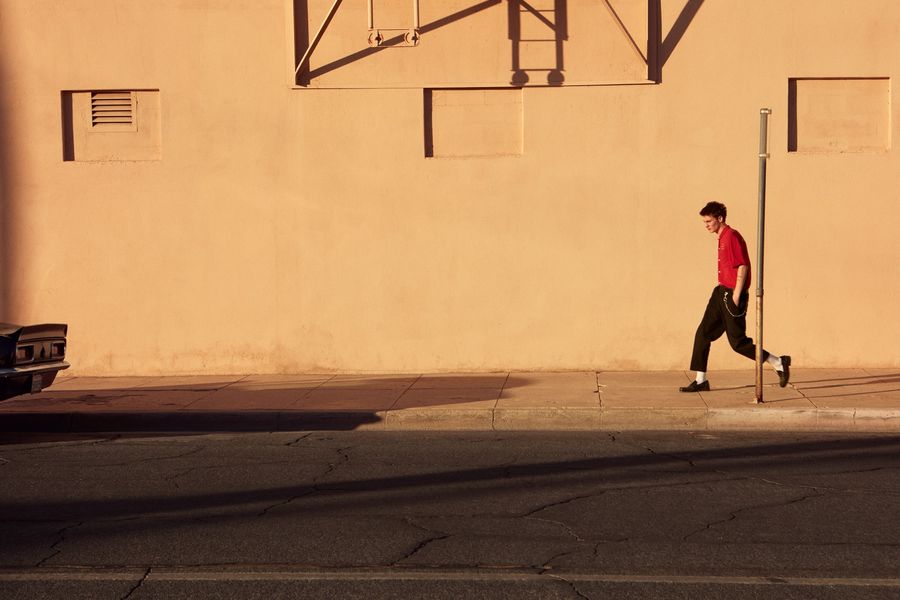 Immagine di un uomo che cammina per strada con indosso pantaloni neri sartoriali e una camicia a maniche corte di colore rosso.