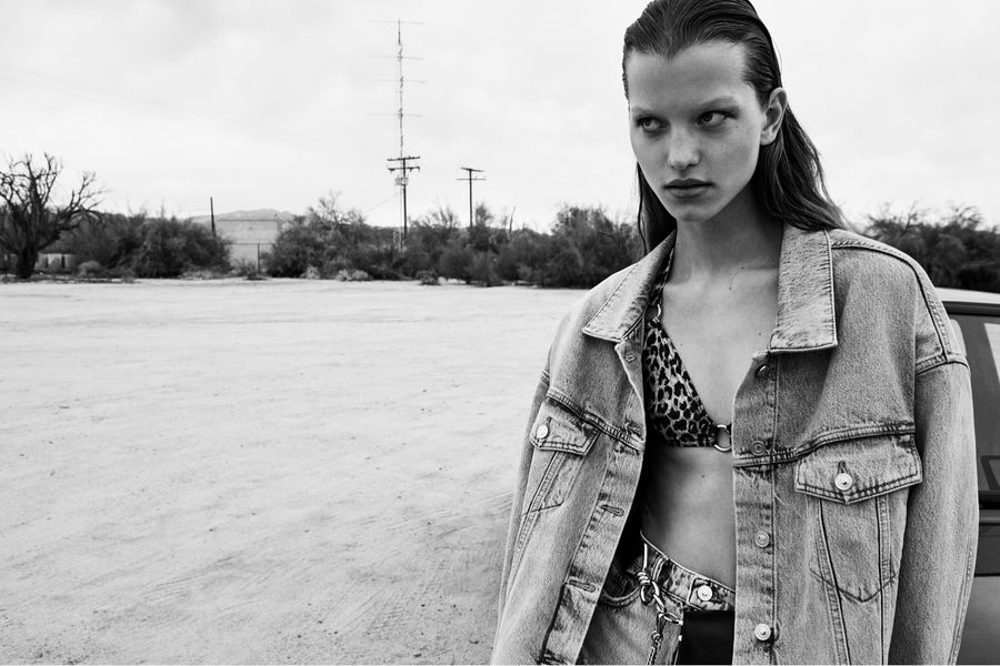 Immagine in bianco e nero di una donna che indossa una giacca di jeans oversize, un bikini leopardato e una gonna di jeans.