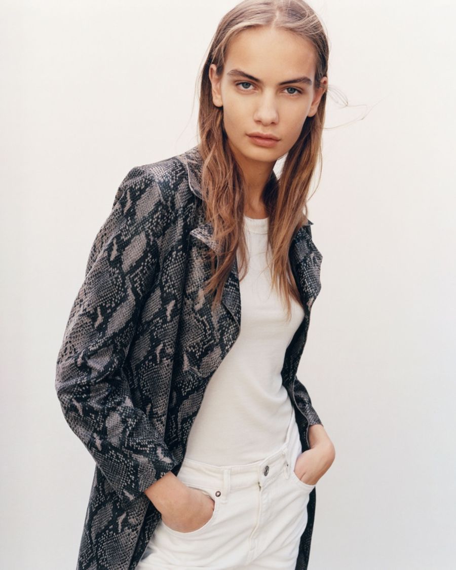 Image of a woman wearing a snake printed trench coat with a white t-shirt and white jeans.