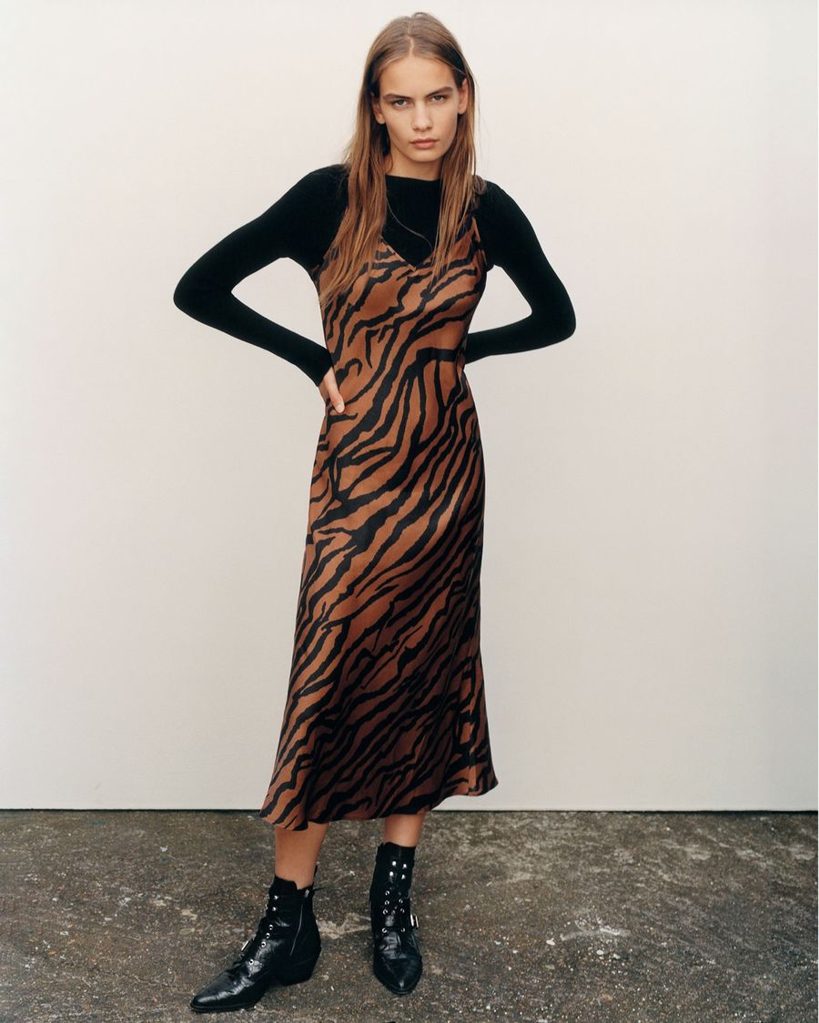 Image of a woman wearing a long zebra printed slip dress over a long sleeve black t-shirt with black leather boots.