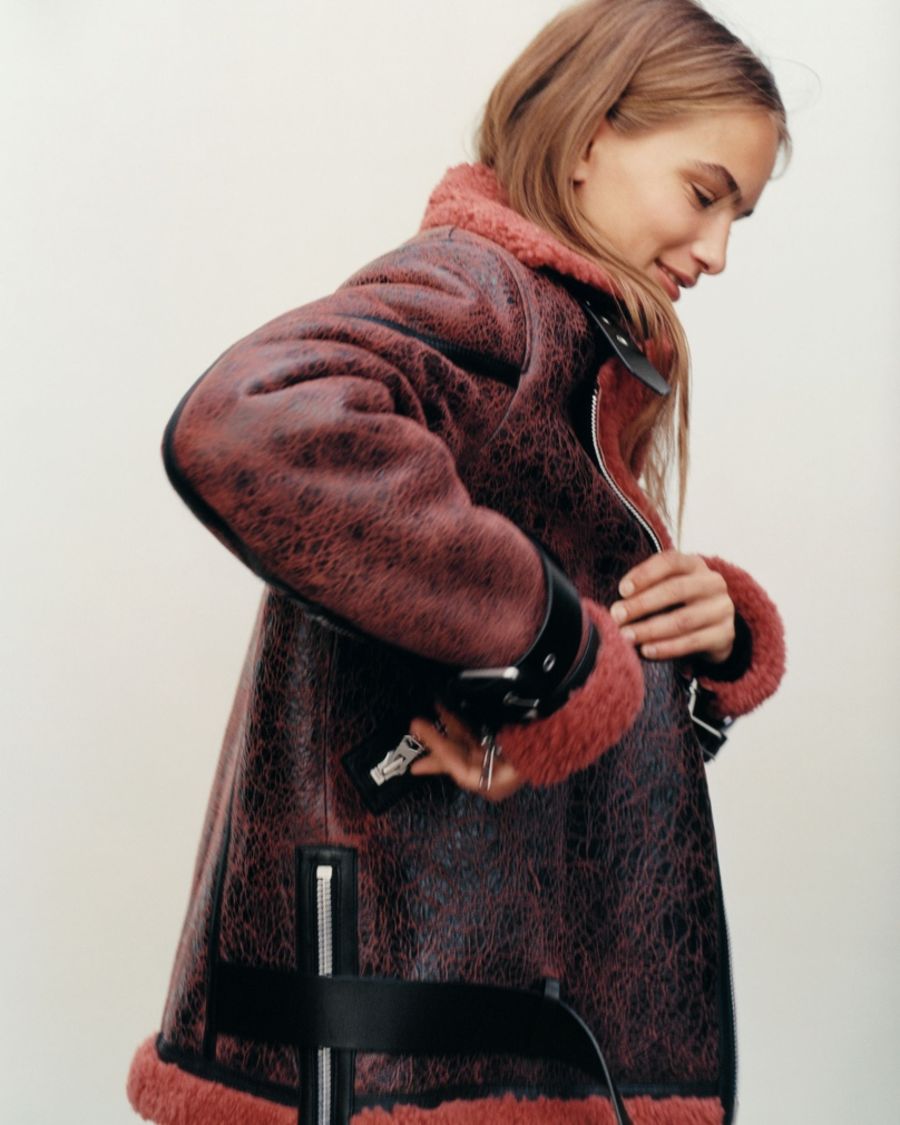Profile portrait of a woman wearing a rusty coloured shearling jacket.