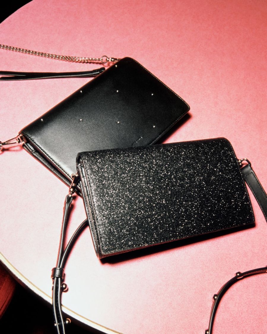Close up of a black studded and a a shiny wallet crossbodies on a red table