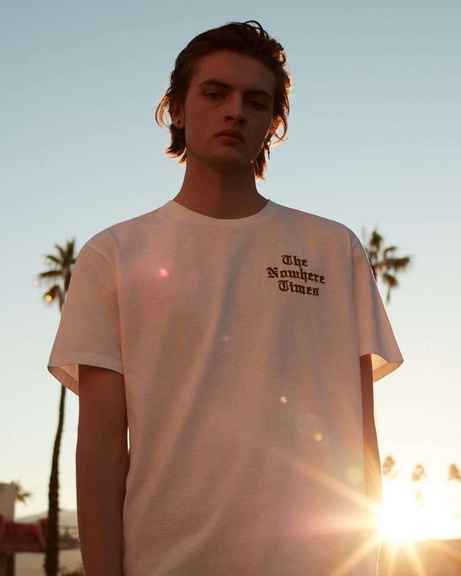 Portrait of a man wearing a white t-shirt with an embroidered logo ont he chest.