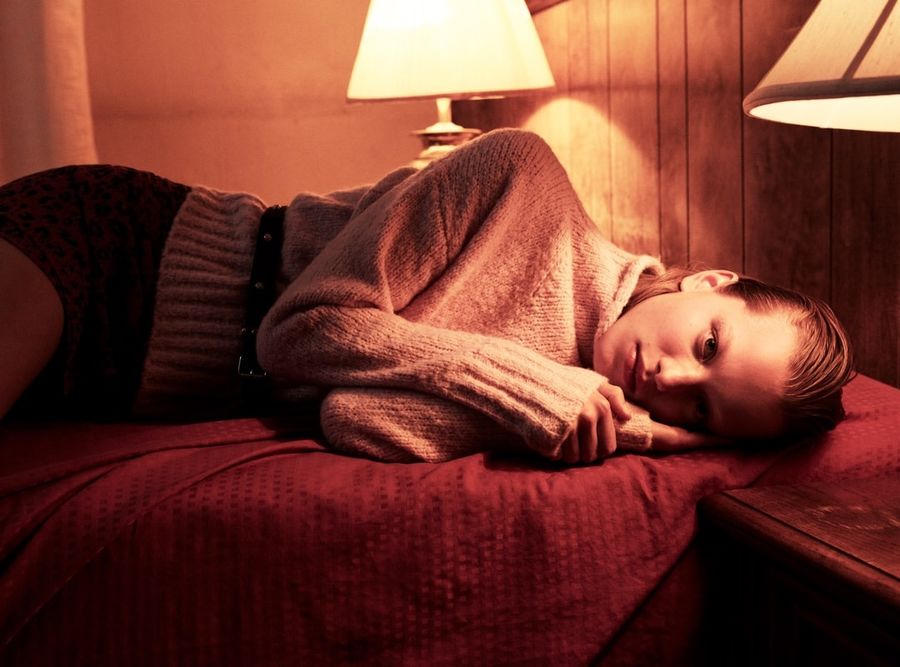 Image of a woman lying on a hotel room bed wearing a pink sweater with a leopard print skirt.