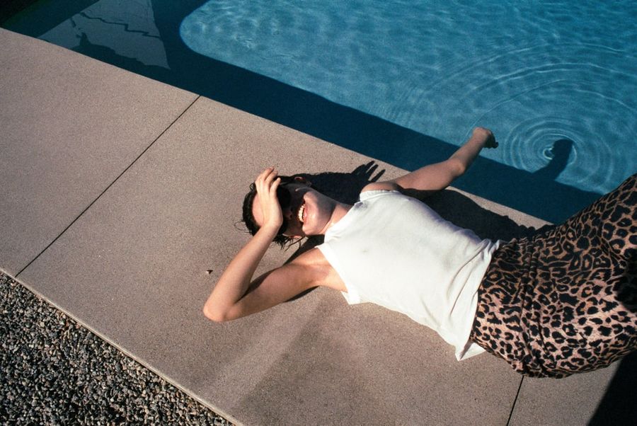 Image of a woman lying by a swimming pool wearing a leopard skirt and white tank top.