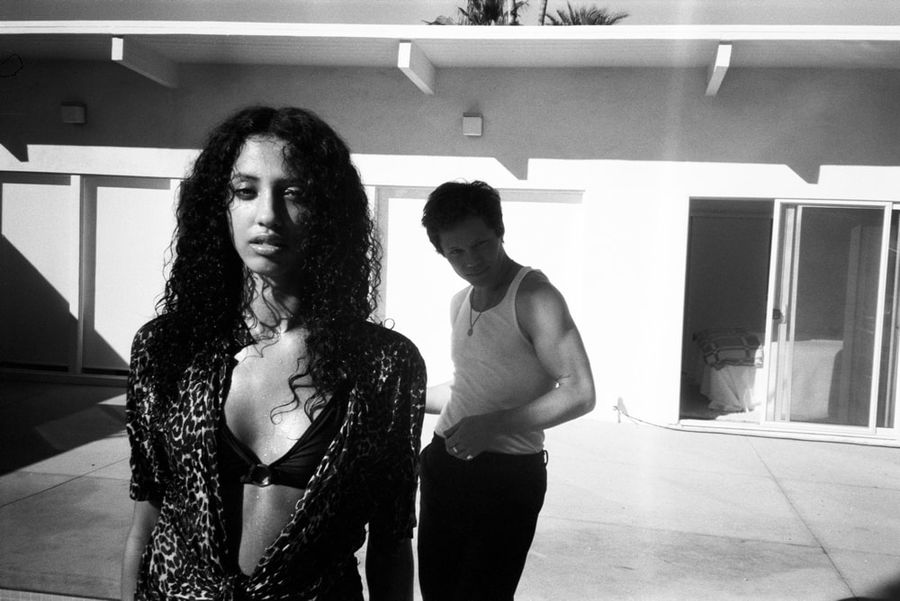 Black and white shot of a woman wearing the Sirena Feline shirt with a man in the background wearing pieces from our latest collection.