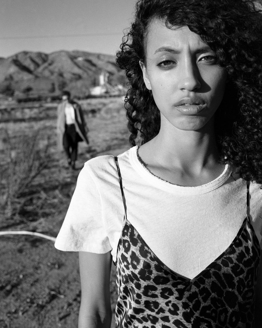 Black and white portrait of a woman wearing a thin strap leopard dress over a white short sleeve t-shirt.
