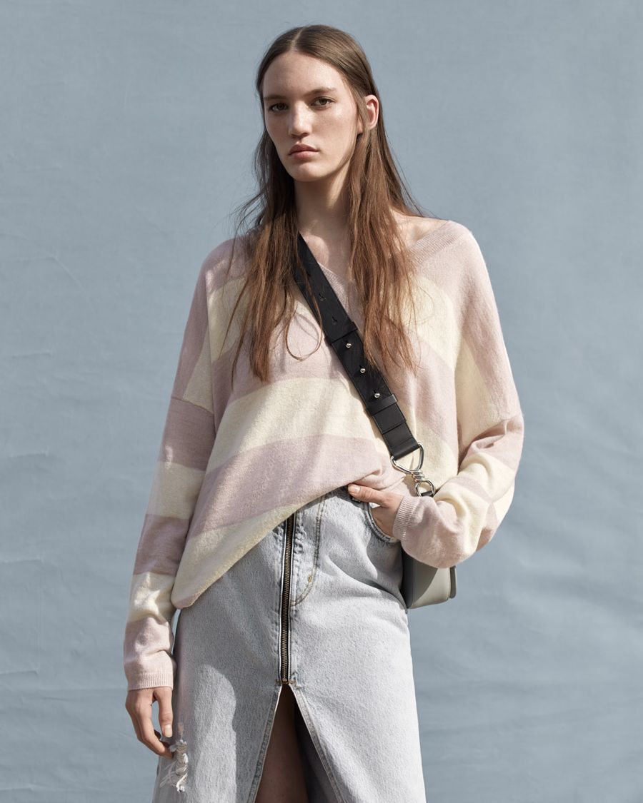 Woman wearing a light pink and beige striped v-neck sweater with a long zipped denim skirt and crossbody bag.